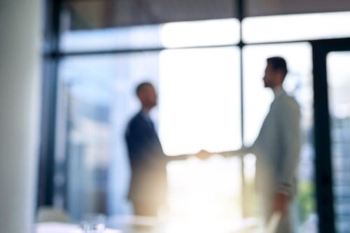 Blurry image of an office with two men shaking hands
